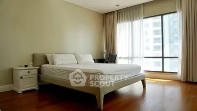 Spacious bedroom with large window and modern furnishings in a high-rise apartment.