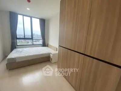 Spacious bedroom with large window offering stunning city views, featuring modern wooden furniture and ample natural light.