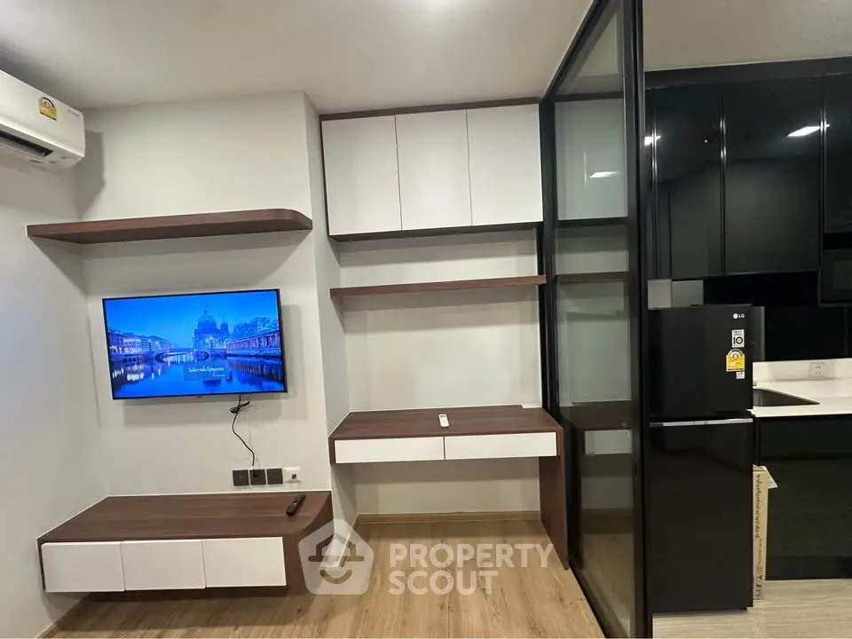 Modern living room with sleek built-in shelves and a wall-mounted TV, adjacent to a stylish kitchen area.