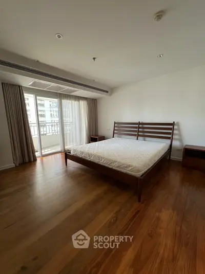 Spacious bedroom with wooden flooring and balcony access in modern apartment.