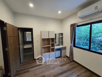 Modern bedroom with wooden flooring, built-in storage, and large window with garden view.