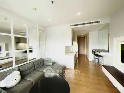 Modern living room with sleek design, featuring a cozy gray sofa, wooden flooring, and a compact kitchen area.