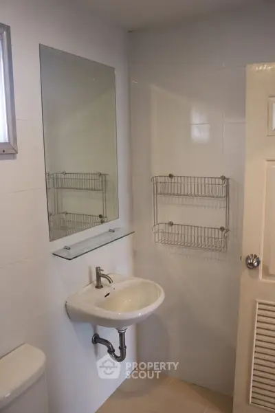 Compact bathroom with sink, mirror, and wall-mounted storage racks.