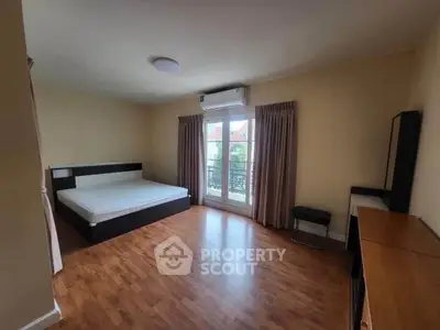 Spacious bedroom with wooden flooring and large window for natural light