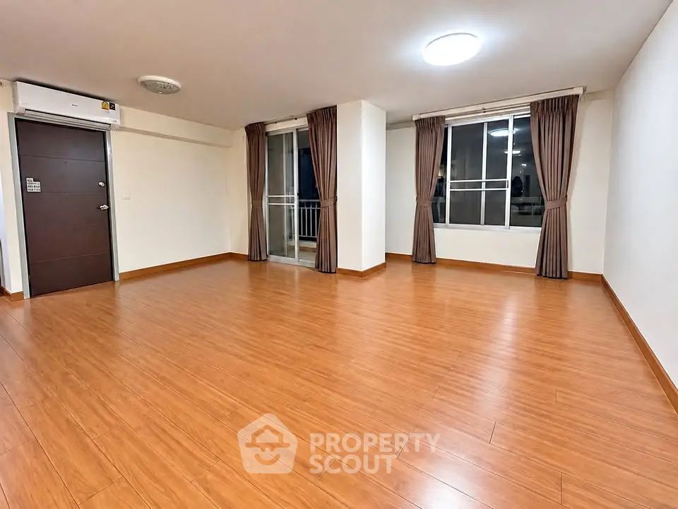 Spacious empty living room with wooden flooring and large windows for natural light.