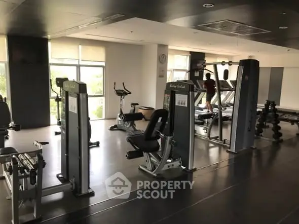 Spacious gym with modern fitness equipment and large windows for natural light.