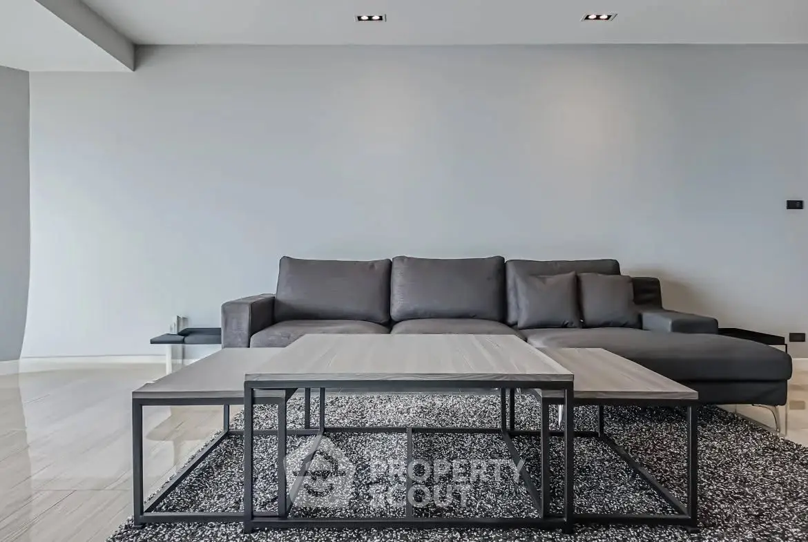 Modern living room with sleek gray sofa and stylish coffee table on a plush rug.