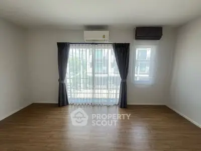Spacious empty room with wooden flooring and large window, ideal for customization.