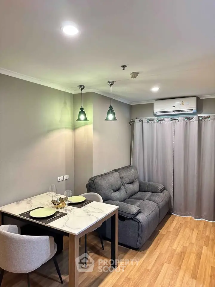 Cozy living room with modern decor and dining area, featuring elegant lighting and wooden flooring.