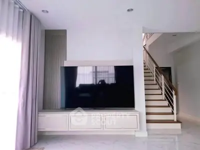 Modern living room with sleek TV setup and elegant staircase, perfect for contemporary living.