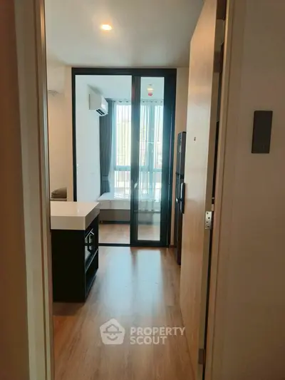 Modern apartment entrance with wooden flooring and sliding glass doors leading to a bright living area.