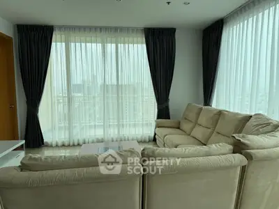 Spacious living room with large windows and plush beige sofa in modern apartment.
