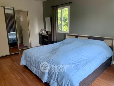 Spacious bedroom with wooden flooring and large window offering natural light.