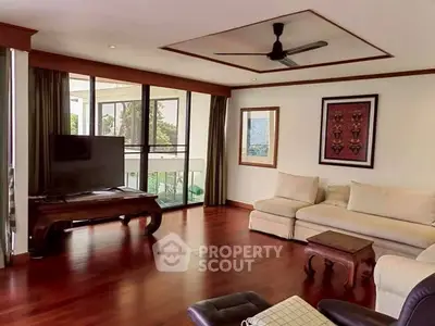 Spacious living room with hardwood floors and large windows opening to a balcony.