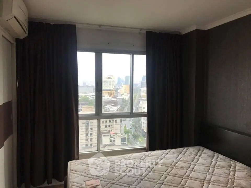 Cozy bedroom with city view from large window, featuring dark curtains and air conditioning.