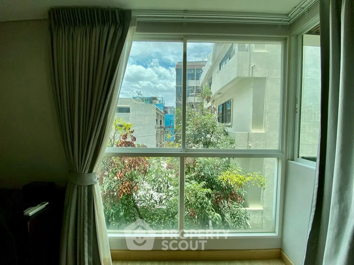 Bright window view with lush greenery and urban buildings, perfect for natural light lovers.