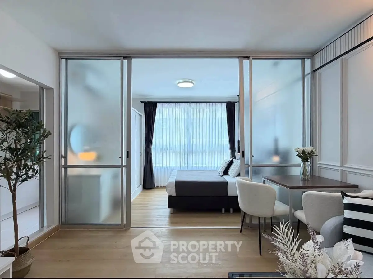Modern open-plan living room with sliding glass doors leading to a stylish bedroom, featuring elegant decor and natural light.