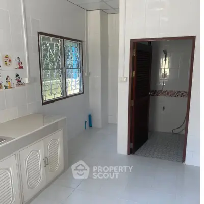 Spacious tiled kitchen with window and adjacent bathroom in modern home.