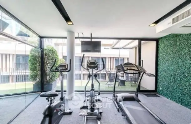 Modern gym with exercise equipment and glass walls overlooking greenery.