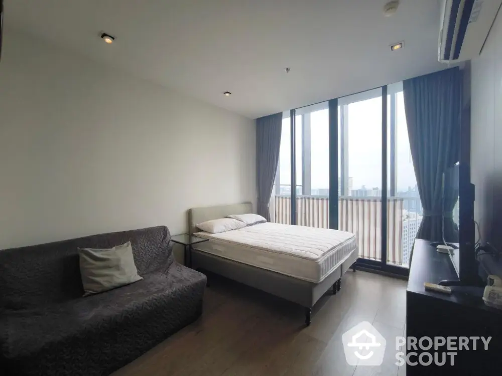 Modern bedroom with large windows and city view, featuring a cozy bed and stylish decor.