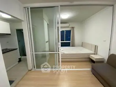 Modern studio apartment with sliding glass partition, cozy bed, and compact kitchen area.