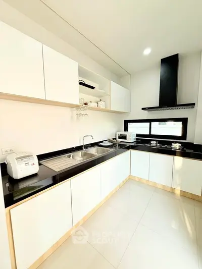 Modern kitchen with sleek black countertops and white cabinetry, featuring built-in appliances and ample natural light.
