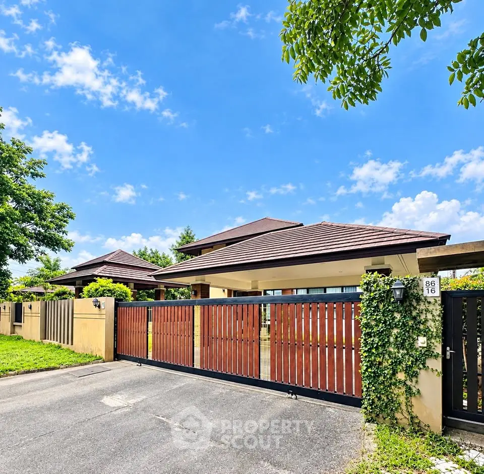 Charming suburban home with gated entrance and lush greenery under a bright blue sky.