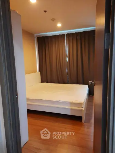 Cozy bedroom with wooden flooring and large window with curtains, perfect for relaxation.