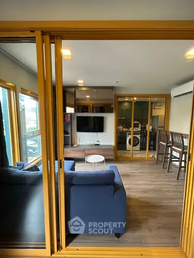 Modern living room with blue sofa, large TV, and open kitchen layout featuring a washing machine.