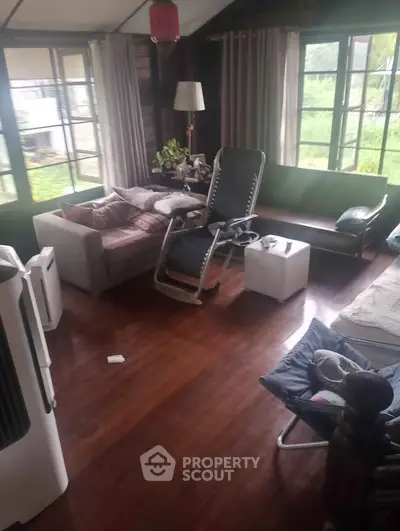 Cozy living room with wooden floors and large windows offering a lush garden view.