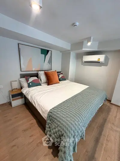 Modern bedroom with stylish decor and air conditioning, featuring a cozy bed and contemporary artwork.