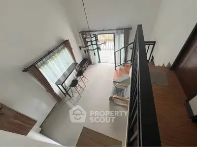 Modern loft-style living room with high ceiling and stylish staircase, featuring large windows and chic furniture.