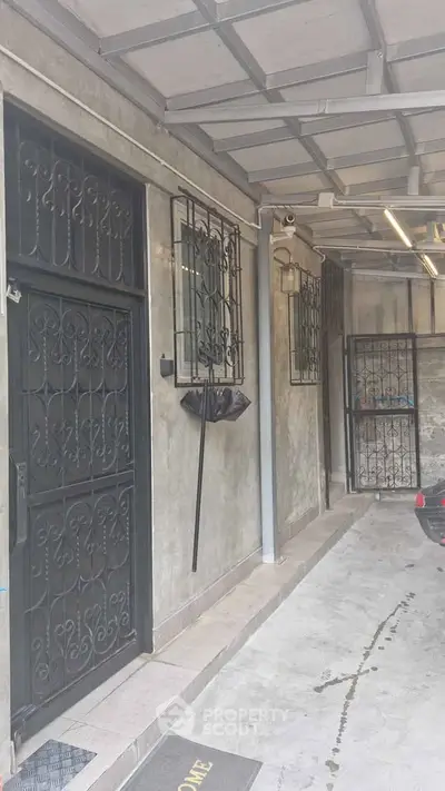 Secure residential entrance with metal gate and covered parking area.