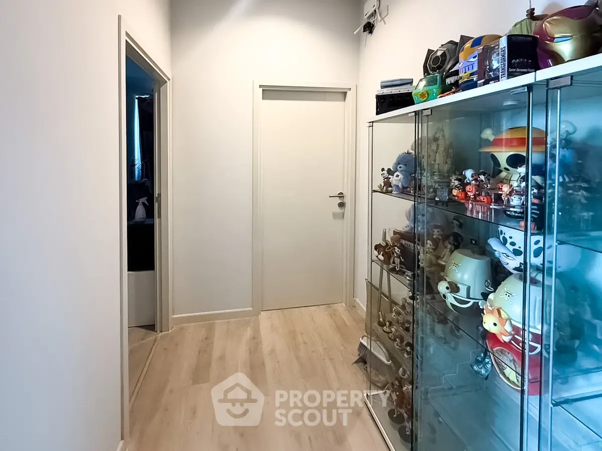 Modern hallway with glass display cabinet showcasing collectibles, sleek wooden flooring, and minimalist design.