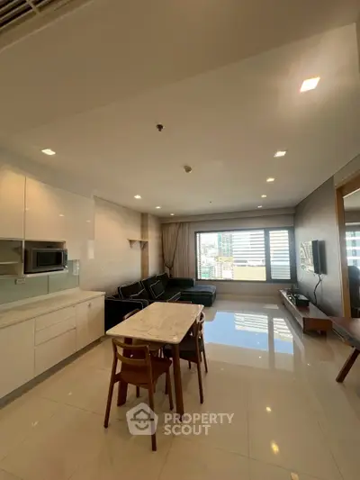 Spacious modern living room with open kitchen and city view, featuring sleek furniture and ample natural light.