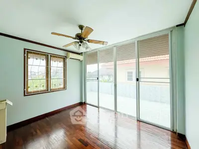 Spacious room with wooden floors and large sliding glass doors leading to a balcony.