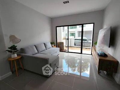 Modern living room with sleek gray sofa and large sliding glass doors opening to balcony.