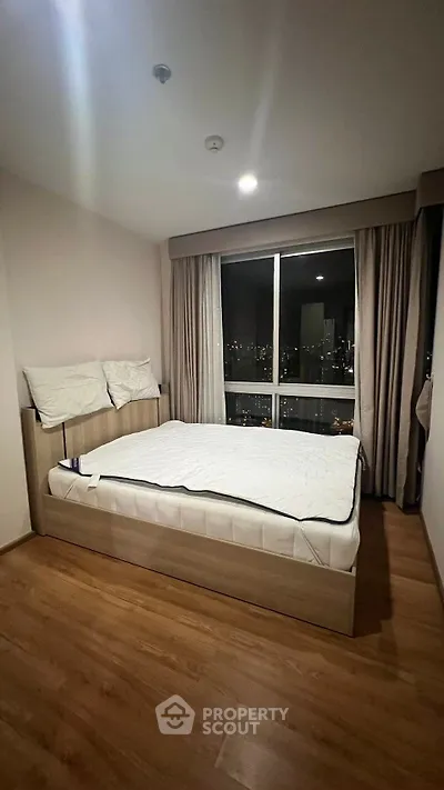 Modern bedroom with city view, featuring a cozy bed and wooden flooring.