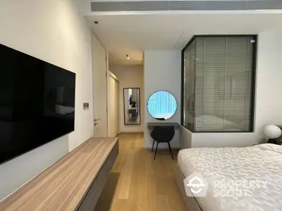 Modern bedroom with stylish decor and large TV, featuring a cozy workspace and elegant design.