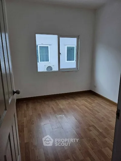 Spacious empty room with wooden flooring and window view, perfect for customization.