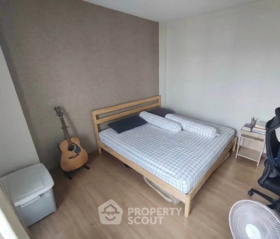 Cozy bedroom with wooden flooring, modern bed, and acoustic guitar for a relaxing ambiance.