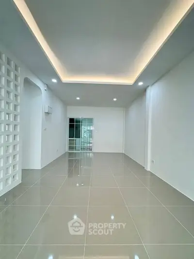 Spacious modern living room with sleek tile flooring and ambient ceiling lighting.