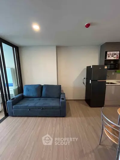 Modern living room with blue sofa and sleek kitchen area, featuring a fridge and dining table.