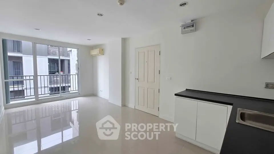 Modern open-plan living room with sleek kitchen and balcony view in a contemporary apartment.