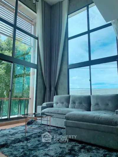 Luxurious living room with floor-to-ceiling windows and plush sofa, offering stunning natural light and views.