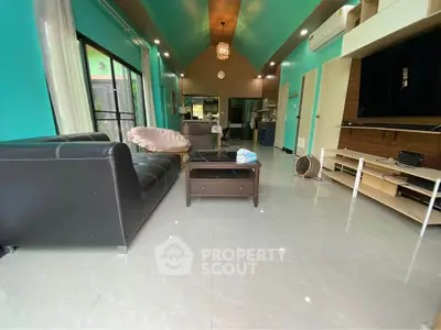 Spacious living room with modern decor and vibrant teal walls, featuring a sleek black leather sofa and open layout.