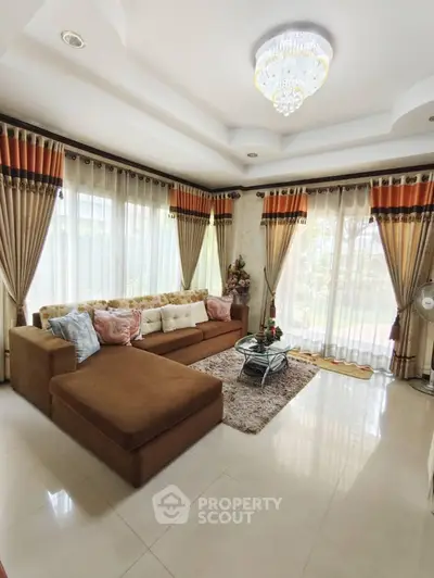 Elegant living room with plush sofa and chandelier, featuring large windows and luxurious curtains.