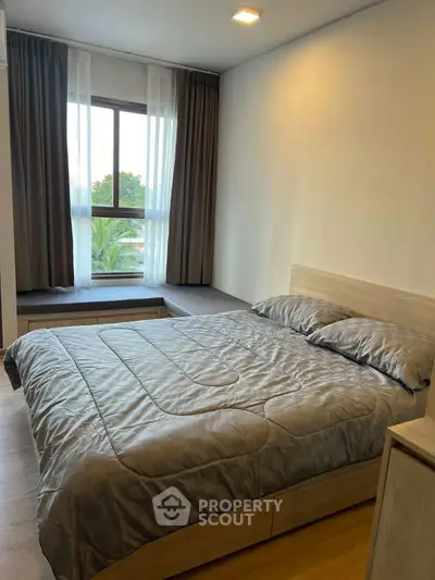 Cozy bedroom with modern decor and large window offering natural light and serene views.