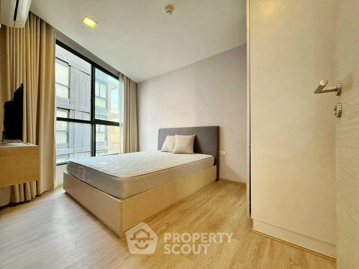 Modern bedroom with large window and wooden flooring in urban apartment