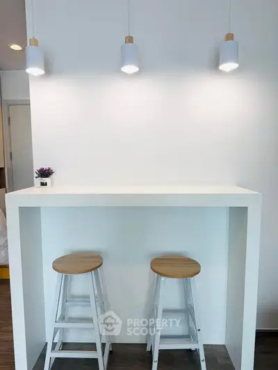Modern minimalist kitchen with white bar counter and stools, perfect for cozy dining.